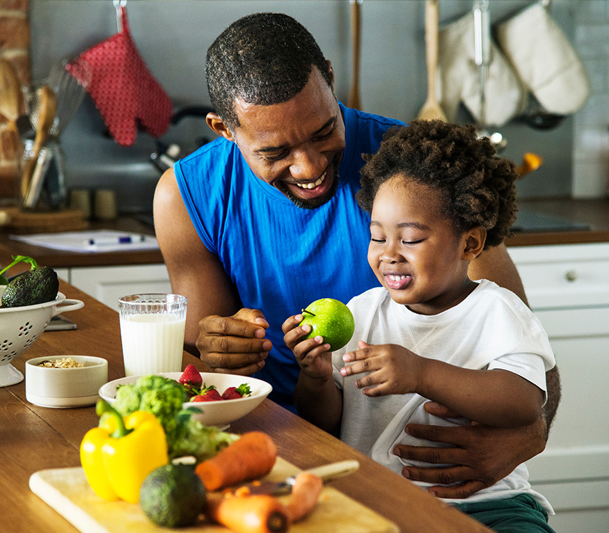 A father sitting with a child eating an apple.